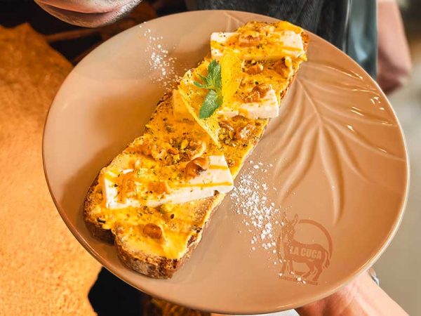 TOSTADA DE MANGO Y FETA: Tostada de pan de centeno con cremoso mascarpone sabor mango, nueces, pistacho, coulis de mango y queso feta.