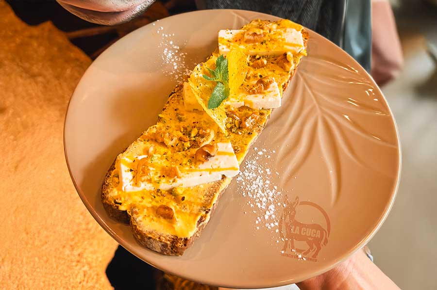 TOSTADA DE MANGO Y FETA: Tostada de pan de centeno con cremoso mascarpone sabor mango, nueces, pistacho, coulis de mango y queso feta.